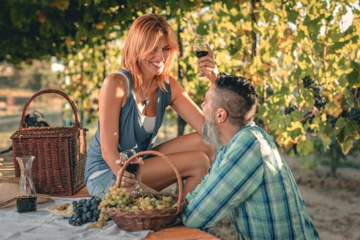Beautiful smiling couple having picnic and tasting wine at a vineyard.