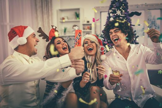 Two young cheerful couple celebrating Christmas with confetti at the home. They are having fun and toasting with champagne. 