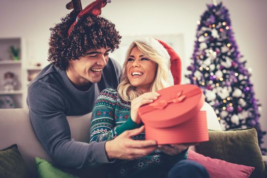 Beautiful young couple celebrating at home. Handsome man is giving his girlfriend a gift box.