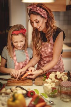 Portrait of happy mother and her daughter cooking together in the kitchen while cutting vegetable.