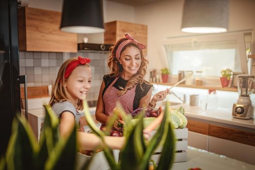 Happy mother and her daughter enjoy making and having healthy meal together at their home kitchen.