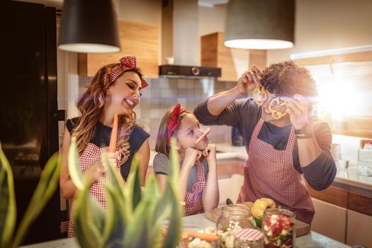Happy parents and their daughter enjoy and having fun in making and having healthy meal together at their home kitchen.