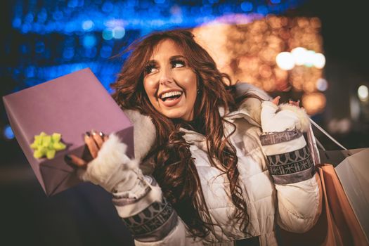 Cheerful young woman with colorful shopping bags using smartphone and having fun in the city street at Christmas time.