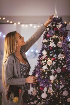 Beautiful smiling young woman decorating christmas tree with Christmas ornament at home.