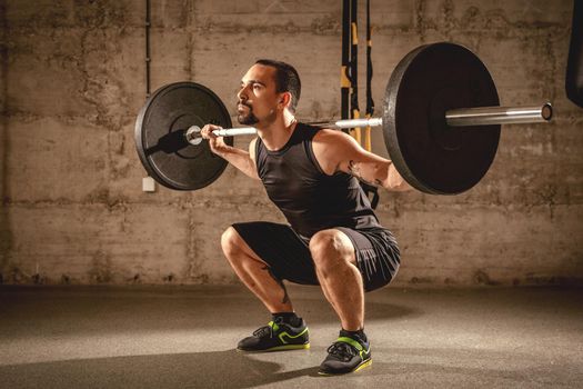 Handsome young muscular man doing squat exercise with barbell at the gym.