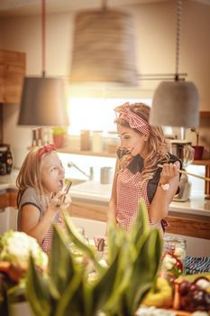 Beautiful woman with her daughter looks happy while preparing meals and tasting vegetable in the kitchen
