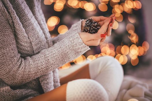 Close-up of a cute young woman holding pinecones in her hands surrounded with Christmas lights. 