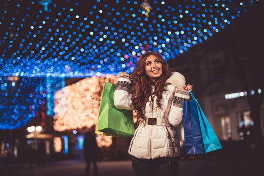 Cheerful young woman with colorful shopping bags having fun in the city street at Christmas time.