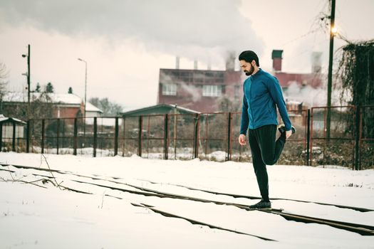 Active young jogging man relaxing legs muscles after training in the ghetto during the winter training outside in. Copy space.