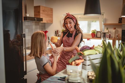 Happy mother and her daughter enjoy and having fun in making and having healthy meal together at their home kitchen.