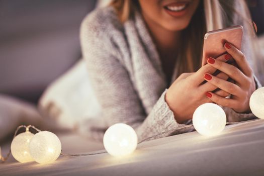 Cute young smiling woman using smarthphone and smiling during cozy Xmas holidays at home.