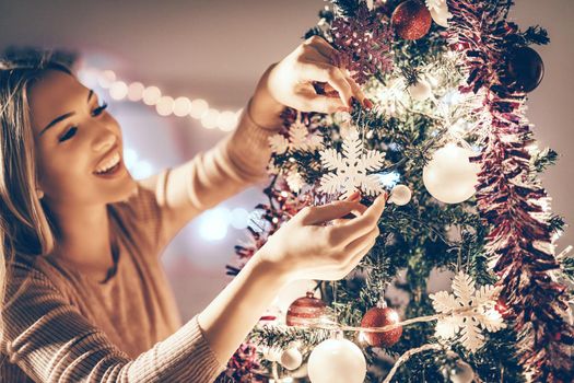 Beautiful smiling young woman decorating christmas tree with Christmas ornament at home.