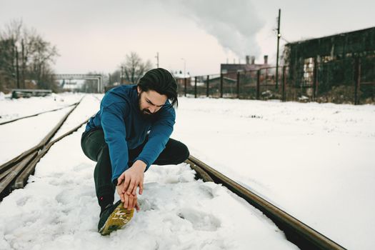 Active young man stretching and doing exercises in the public place among old railroad during the winter training outside in.