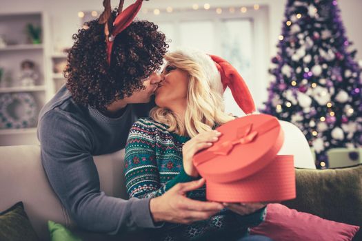 Young romantic couple hugging and kissing in Christmas time. Handsome man is giving his girlfriend a gift box