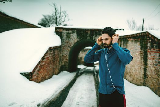 A male runner with headphones on his ears prepare to run in the public place during the winter training outside in. Copy space.