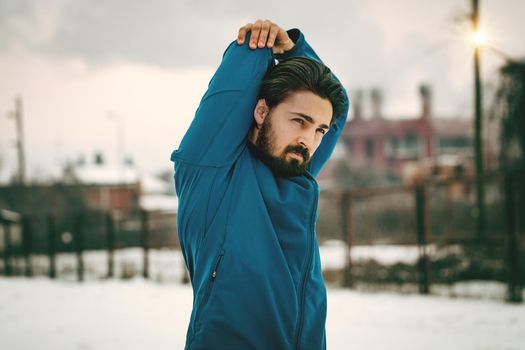 Active young man stretching and doing exercises in the old factory place among old railroad during the winter training outside in. Copy space. 