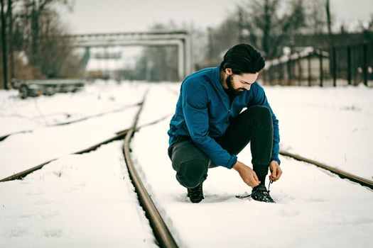 Urban jogger tying running shoes and making pause during stretching and exercises in the winter training outside in.