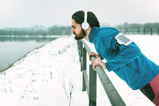 Young man athlete doing push ups and doing exercises during the winter training outside beside the river. Copy space.