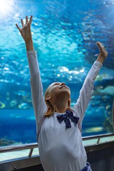 Young girl standing outstretched against aquarium glass fascinated by ocean world.
