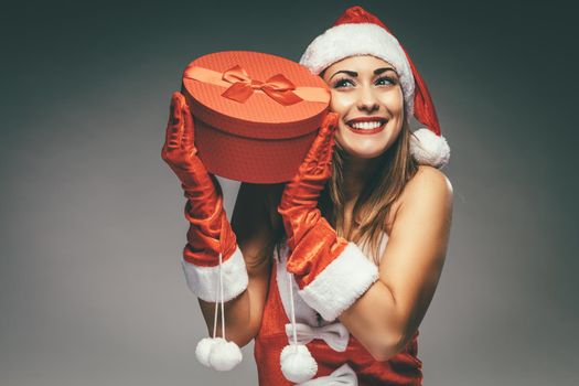 Beautiful young smiling woman in Santa Claus costume holding red present and having fun.