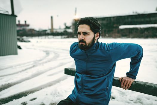 Active young  man stretching and doing exercises in the public place among old railroad during the winter training outside in. Copy space. 
