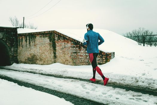 A male runner with headphones on his ears running in the public place during the winter training outside in. Copy space.