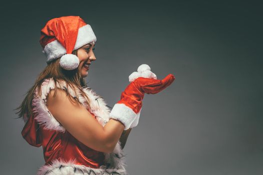 Portrait of a beautiful young smiling woman in Santa Claus costume holding snowballs.