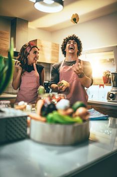 Happy young couple enjoys and having fun preparing vegetables and making healthy meal together at their home kitchen.  