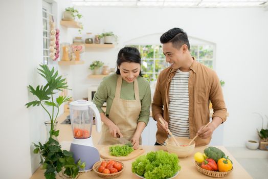 Portrait of happy young Asian couple cooking together in the kitchen at home.