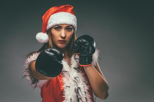 Beautiful young angry woman in Santa Claus costume with boxing gloves.