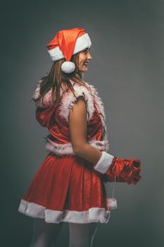 Beautiful young smiling woman in Santa Claus costume holding red present.