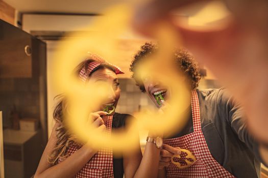 Happy young couple enjoys and having fun in eating slices of capsicum and making healthy meal together at their home kitchen.