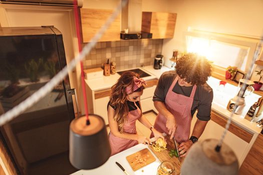 Cute couple is putting vegetables in a jar and smiling while making pickle in kitchen at home