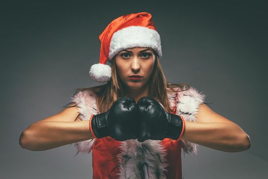 Beautiful young angry woman in Santa Claus costume with boxing gloves.