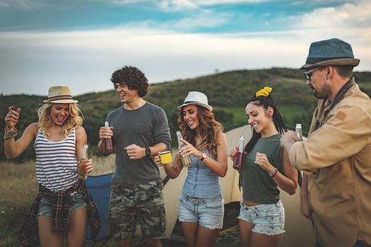 Happy young friends enjoy a nice day in nature. They're holding beer bottles, laughing and talking happy to be together.