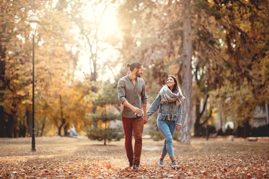 Beautiful smiling couple enjoying in sunny city park in autumn colors looking each other.