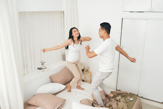 Dancing on the bed. Full length of beautiful young couple holding hands and smiling while dancing on the bed at home