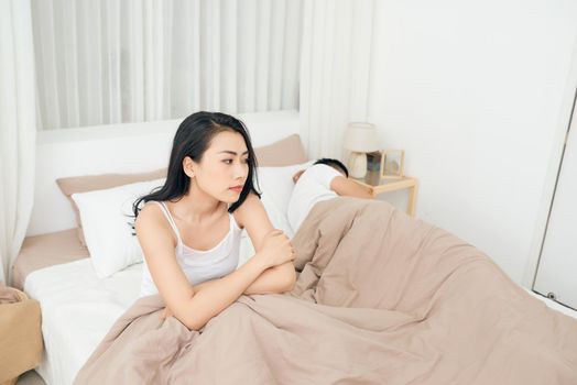 Unhappy Young Couple Sitting On Bed In Bedroom