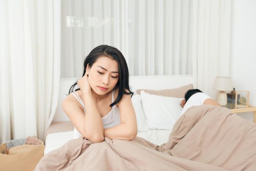 We have a problem. Young upset girl sitting on the edge of the bed, against her boyfriend, lying in bed.