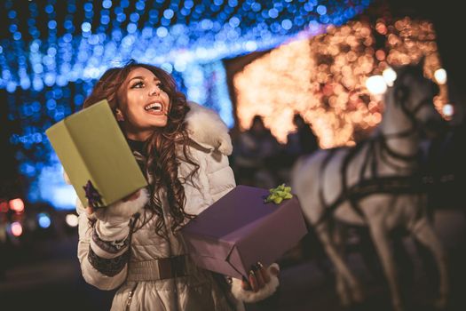 Cheerful young woman with colorful shopping bags using smartphone and having fun in the city street at Christmas time.