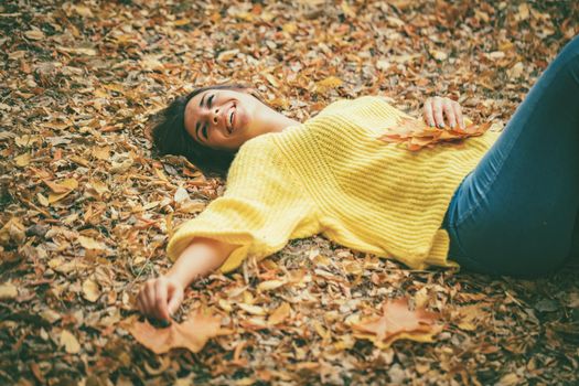 Beautiful young woman in sunny forest in autumn colors. She is lying down on the fall meadow and enjoying.