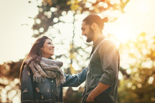 Beautiful smiling couple enjoying in sunny city park in autumn colors looking each other.