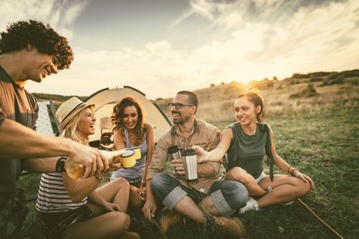 Happy young friends enjoy a nice day in nature. They're grilling sausages, eating, drinking  champagne, laughing and talking happy to be together.   