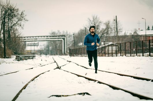 Active young man running and doing exercises across the old railroad during the winter training outside in. Copy space.