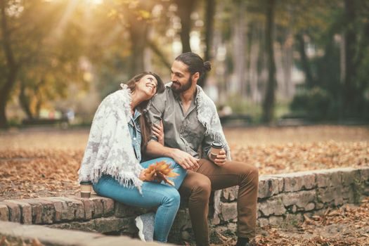 Beautiful smiling couple enjoying in sunny city park in autumn colors looking each other. They are having fun with yellow leaves.