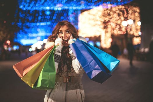 Cheerful young woman with colorful shopping bags having fun in the city street at Christmas time.