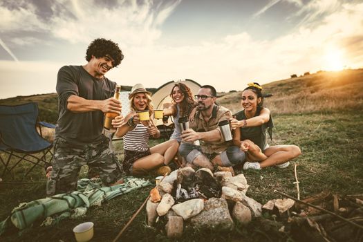 Happy young friends enjoy a nice day in nature. They're grilling sausages, eating, drinking  champagne, laughing and talking happy to be together.   