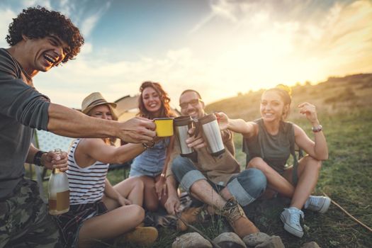 Happy young friends enjoy a nice day in nature. They're grilling sausages, eating, drinking  champagne, laughing and talking happy to be together.   