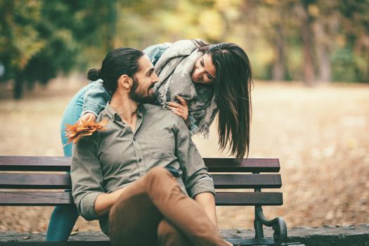 Beautiful smiling couple enjoying in sunny city park in autumn colors looking each other. They are having fun with yellow leaves.