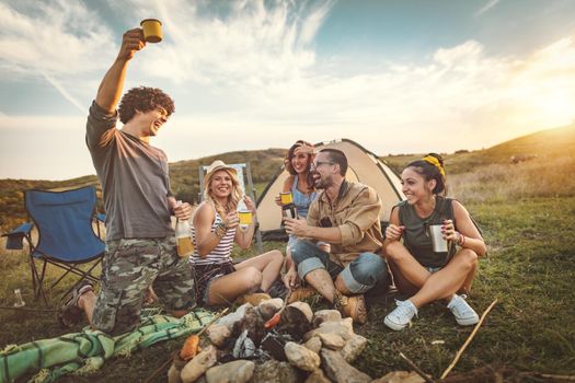 Happy young friends enjoy a nice day in nature. They're grilling sausages, eating, drinking  champagne, laughing and talking happy to be together.   